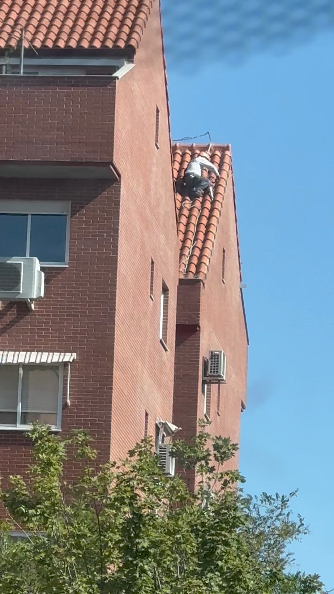 Trabajador reparando tejado de tejas en edificio de ladrillo en Madrid.
