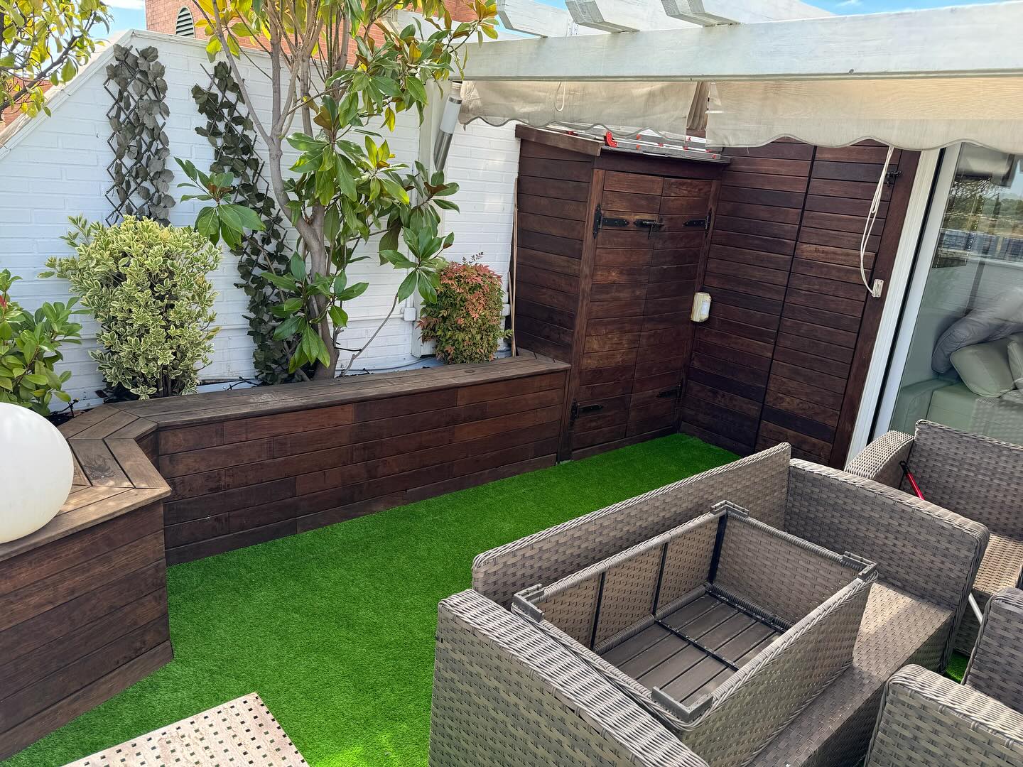 Terraza con césped artificial, muebles de mimbre y jardineras de madera en Madrid.